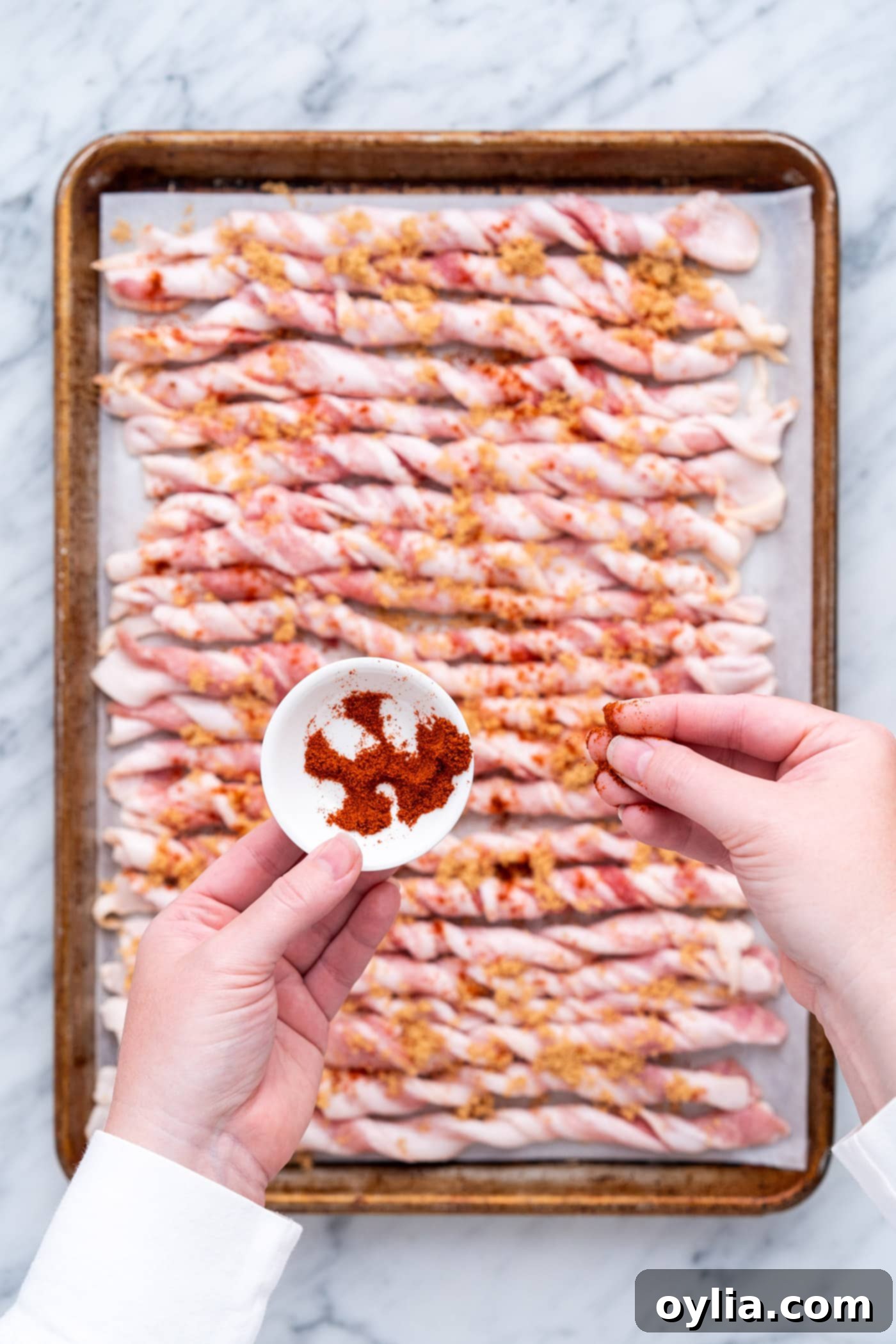 Adding a sprinkle of cayenne pepper over the brown sugar-coated bacon twists.