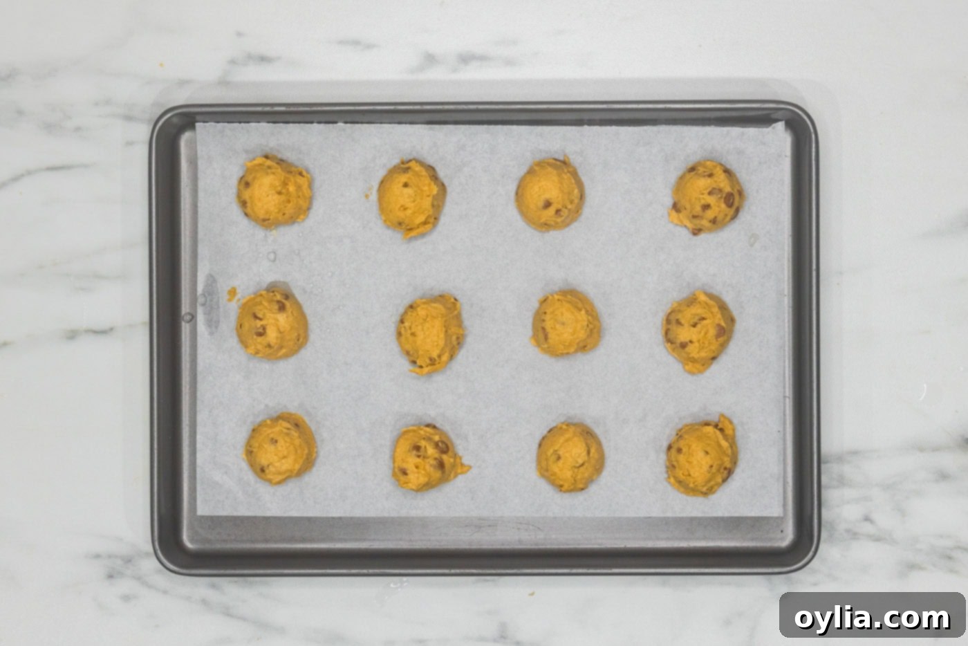 Pumpkin cinnamon chip cookie dough balls neatly placed on a lined baking sheet, ready for the oven.