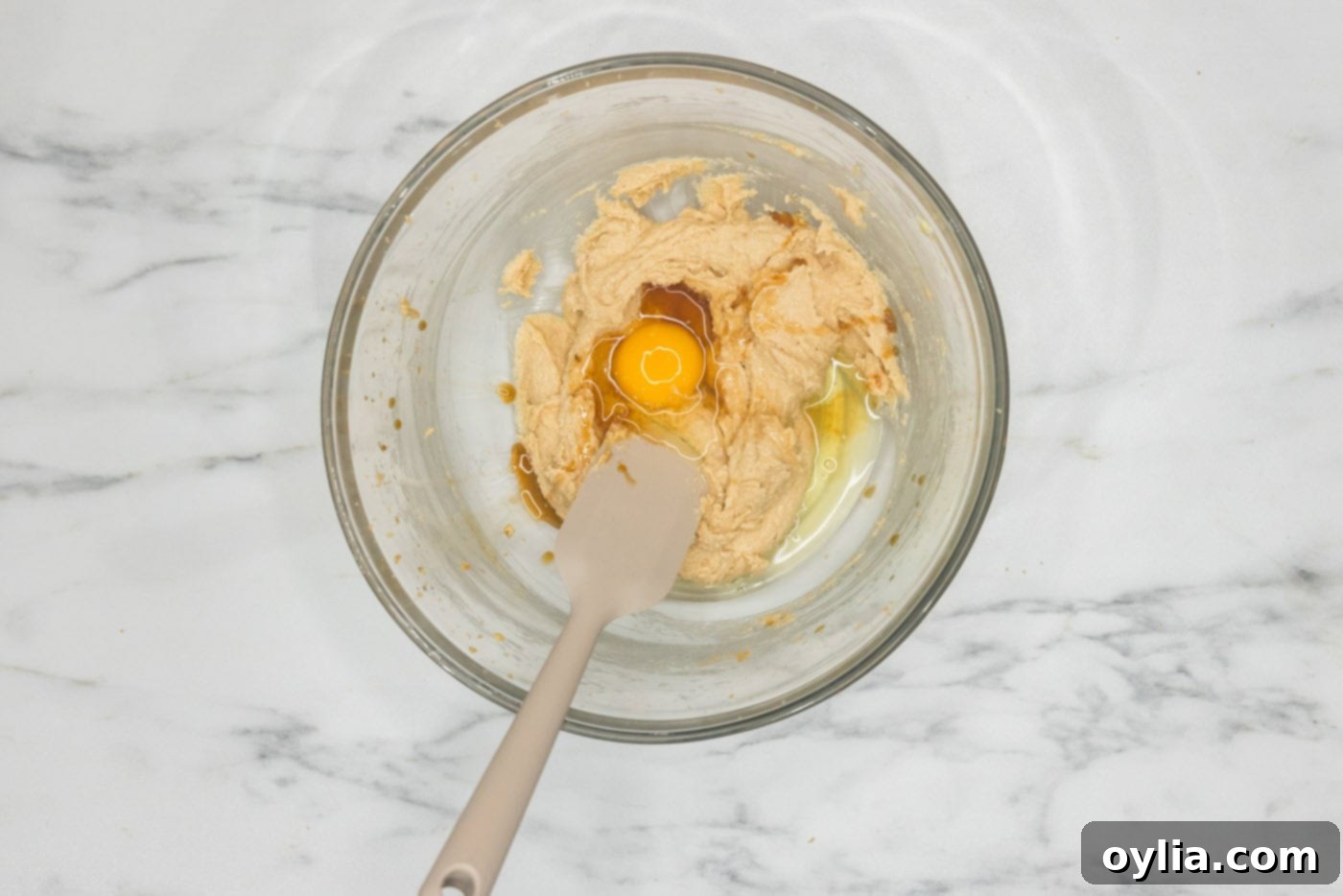 Rubber spatula in a bowl with egg, butter, and sugar mixture, ready for mixing.