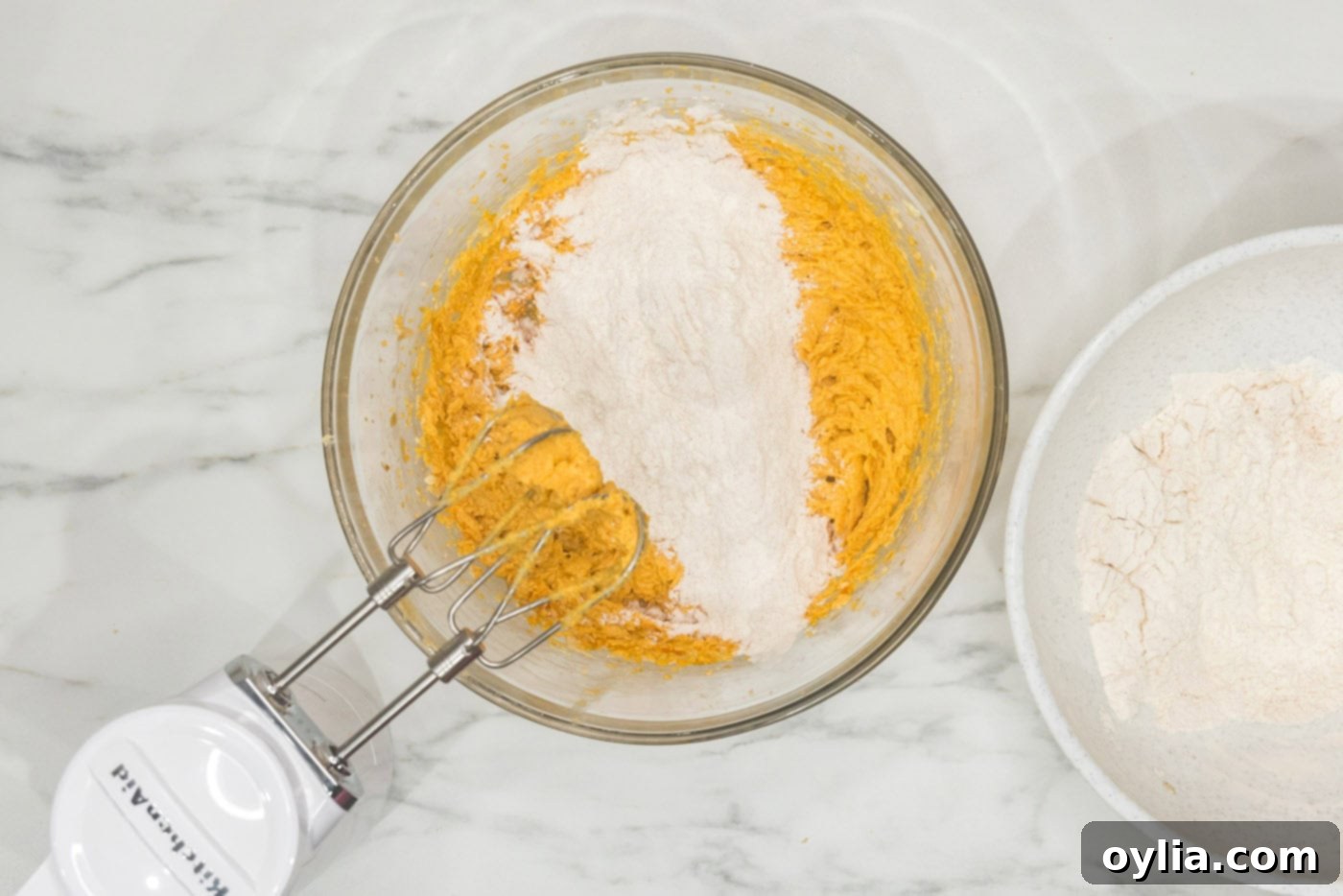 Adding dry ingredients to wet ingredients in a bowl with a hand mixer, demonstrating the careful combination process.