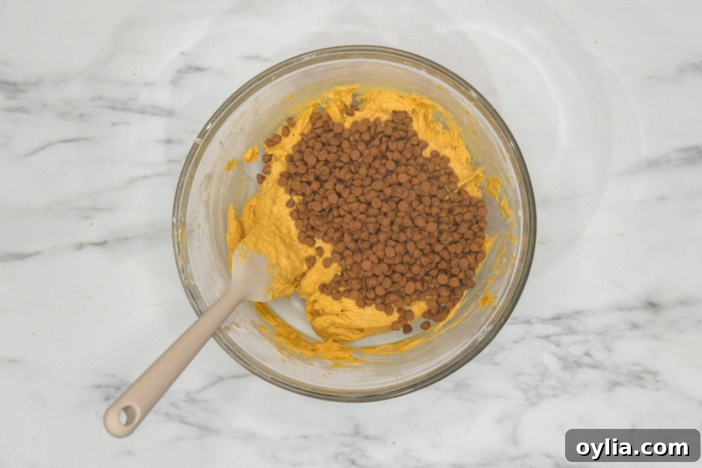 Adding cinnamon chips to a bowl of pumpkin cookie dough, showing the final step before baking.