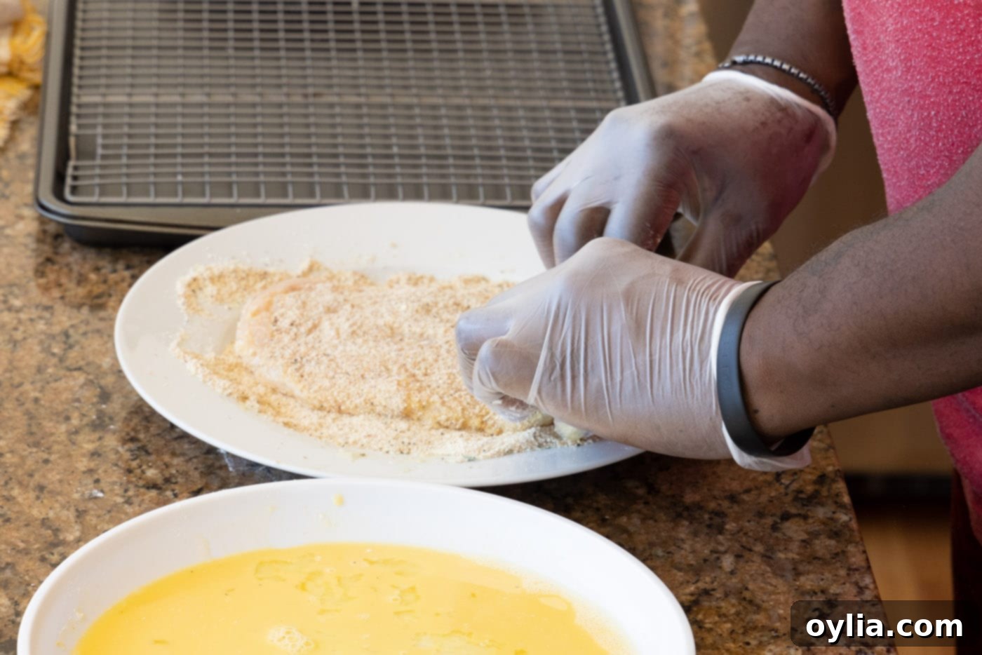 A hand pressing an egg-coated chicken cutlet into a bed of seasoned breadcrumbs for a complete and even coating.