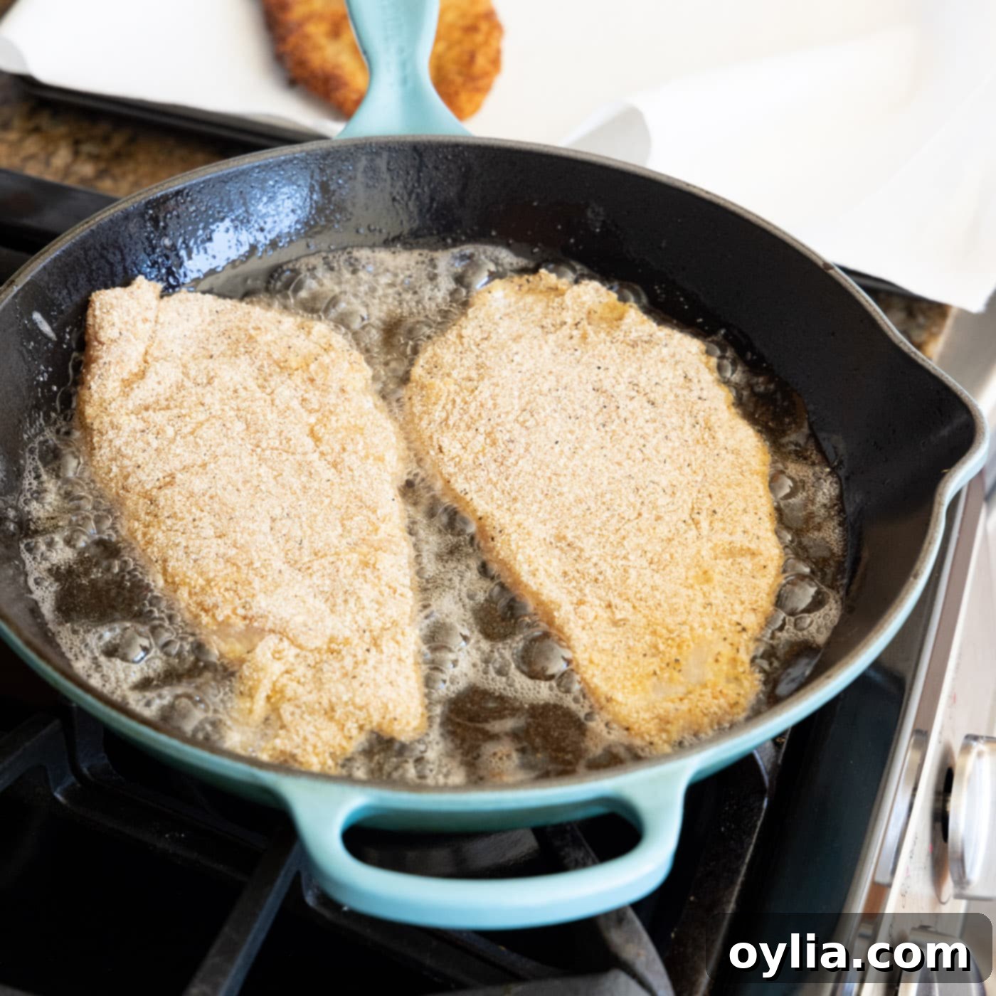 Chicken cutlets sizzling and browning in a hot skillet with olive oil, showing the first side cooking to golden perfection.