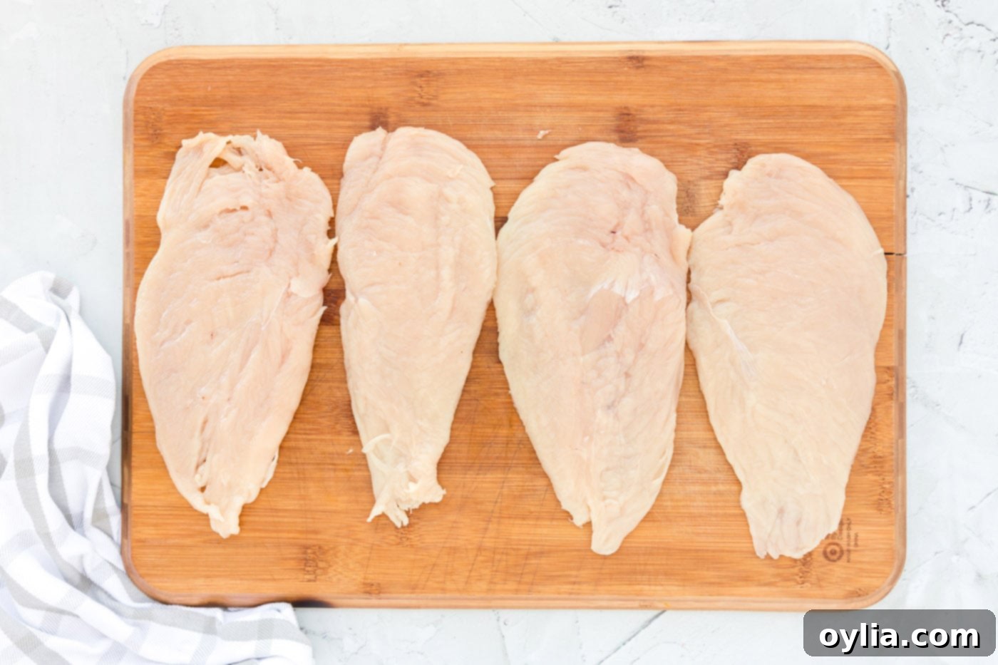 Pounding chicken cutlets between plastic wrap with a meat mallet to achieve an even 1/4 inch thickness for Milanese.