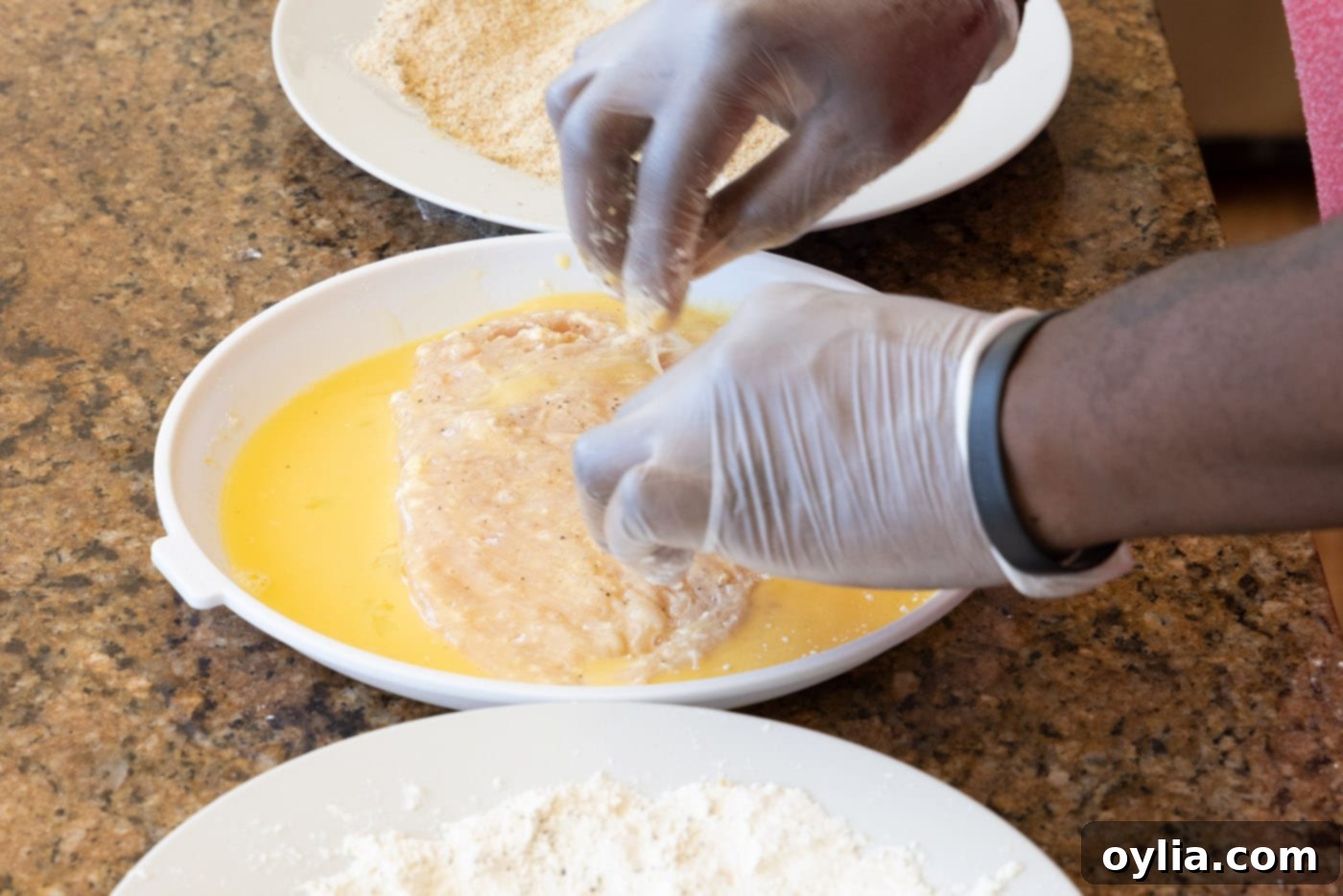 Dredging a flour-coated chicken cutlet into the egg wash, ensuring even coverage before moving to breadcrumbs.