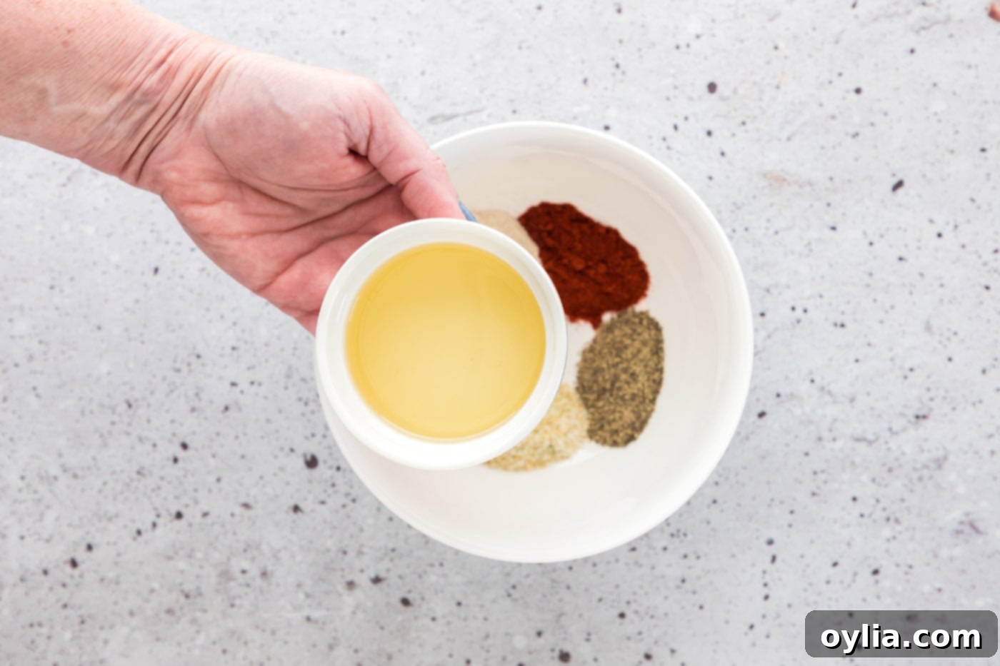 adding olive oil to seasoning mix in a bowl