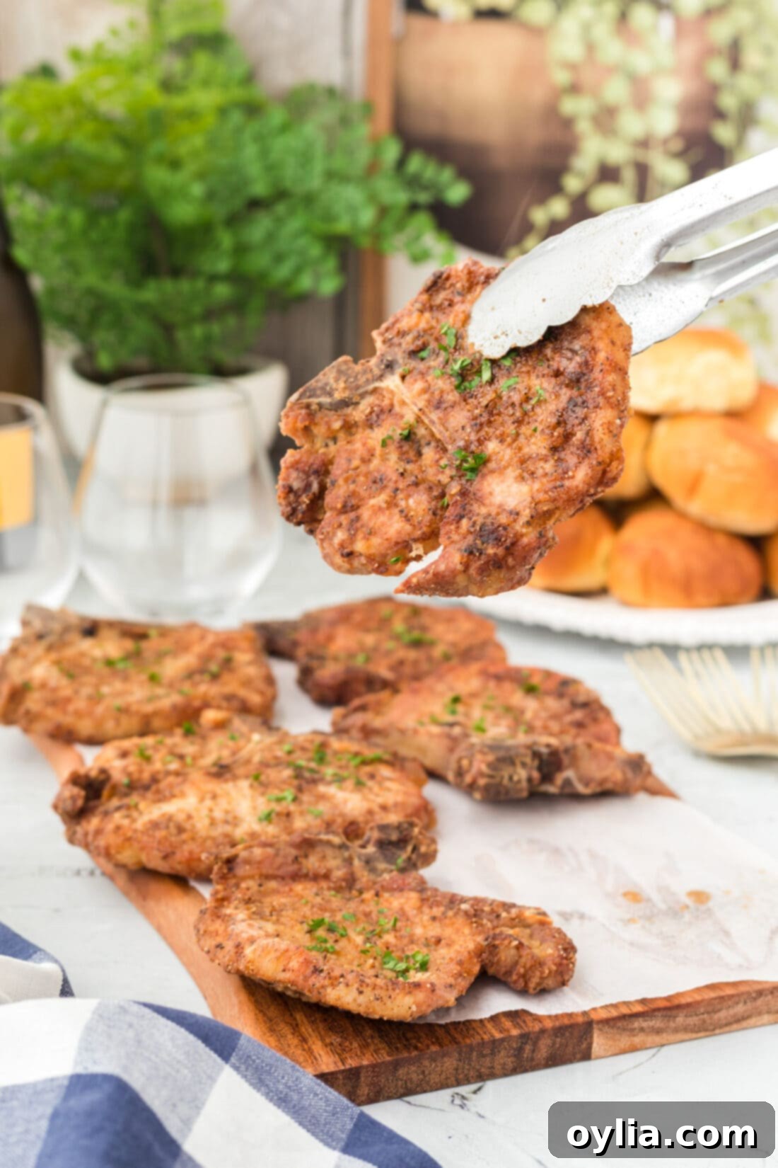 Tongs lifting a crispy fried pork chop from a skillet