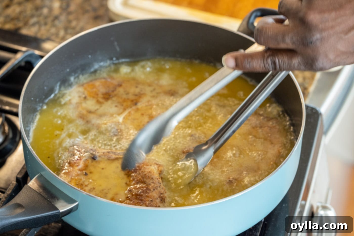 Tongs flipping a frying pork chop in a skillet to reveal a golden brown crust