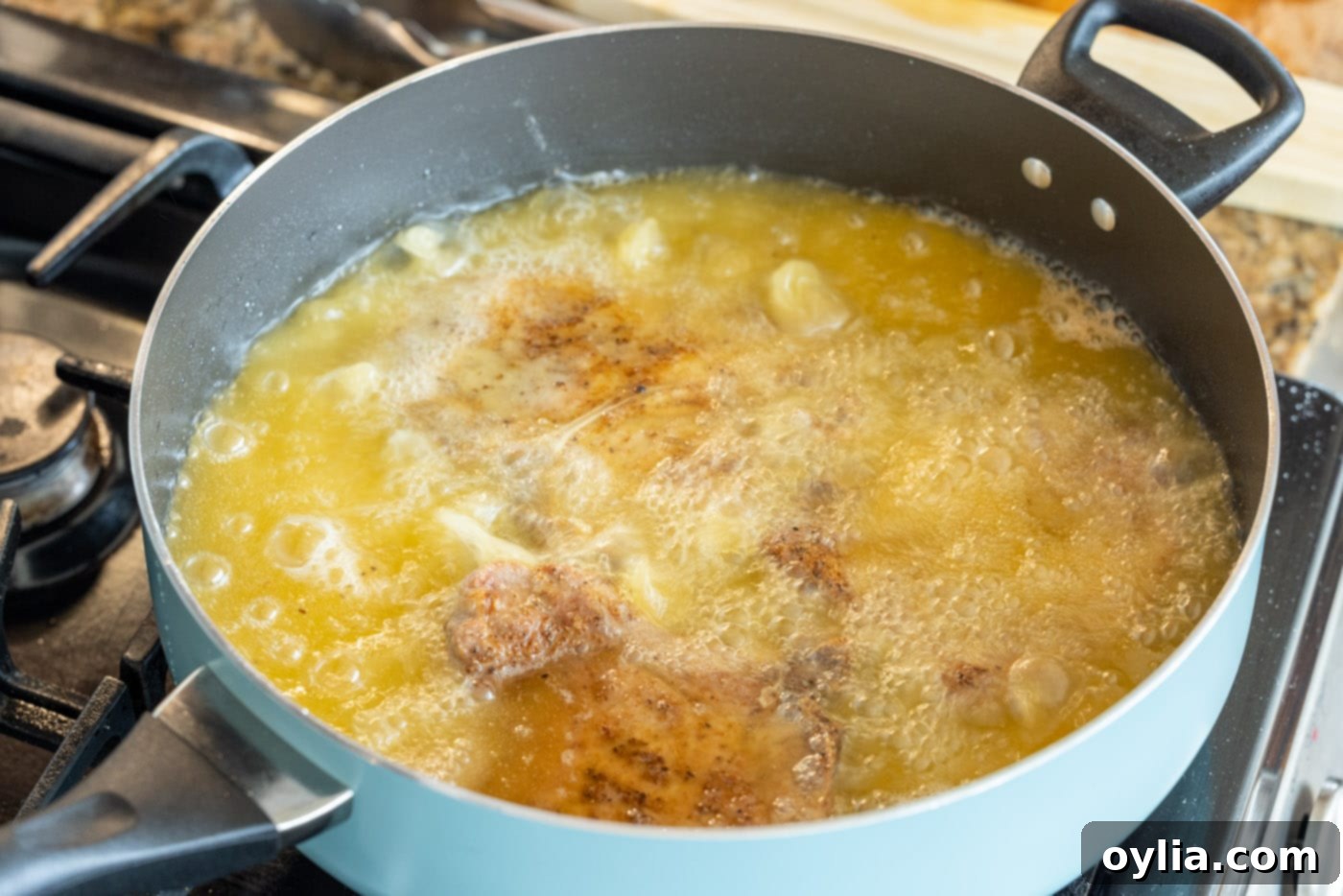 Multiple pork chops frying in a hot skillet, bubbling oil visible