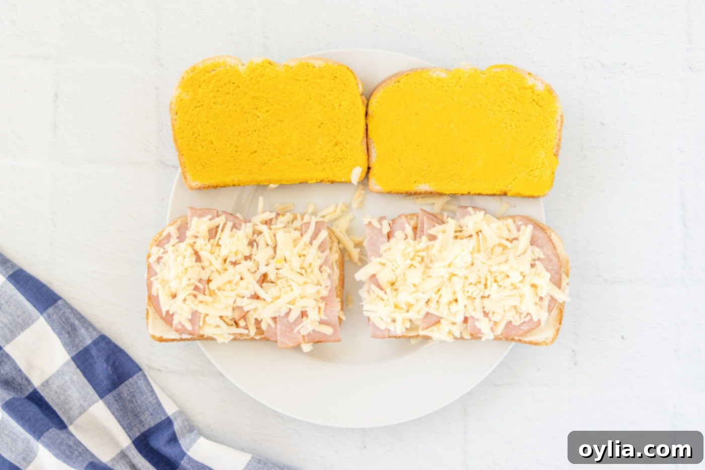 shredded gruyere cheese on top of mayo and ham on bread