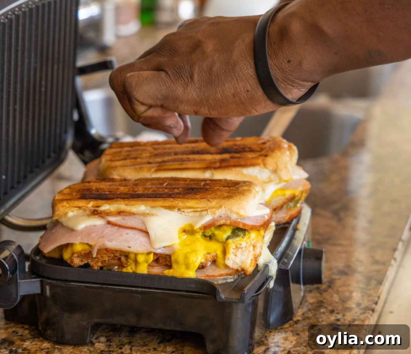 The golden-brown Cuban sandwich being carefully removed from the panini press