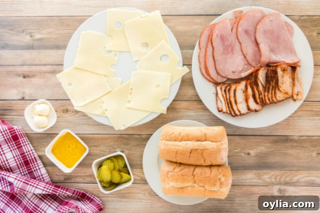 Arrangement of fresh ingredients for a Cuban Sandwich, including bread, pork, ham, cheese, pickles, and mustard