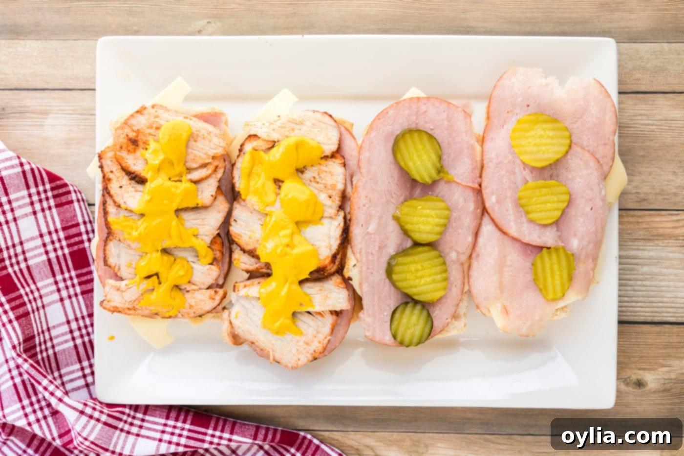 Yellow mustard being applied to the pork tenderloin layer of the Cuban sandwich