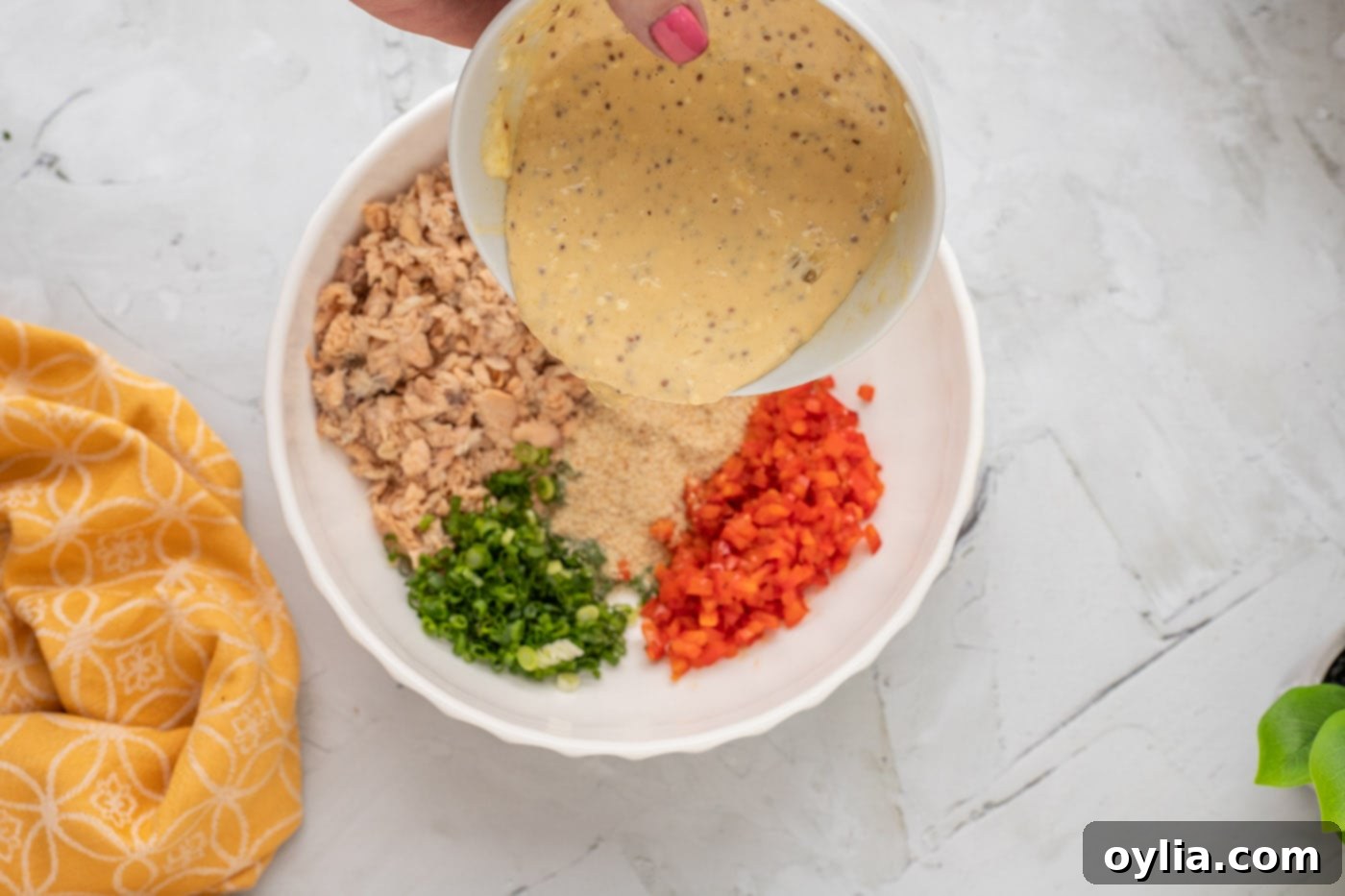 Pouring mayonnaise mixture over salmon patty ingredients