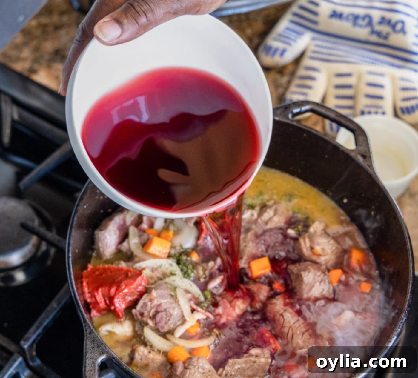 Pouring red wine into the Beef Bourguignon mixture in a Dutch oven