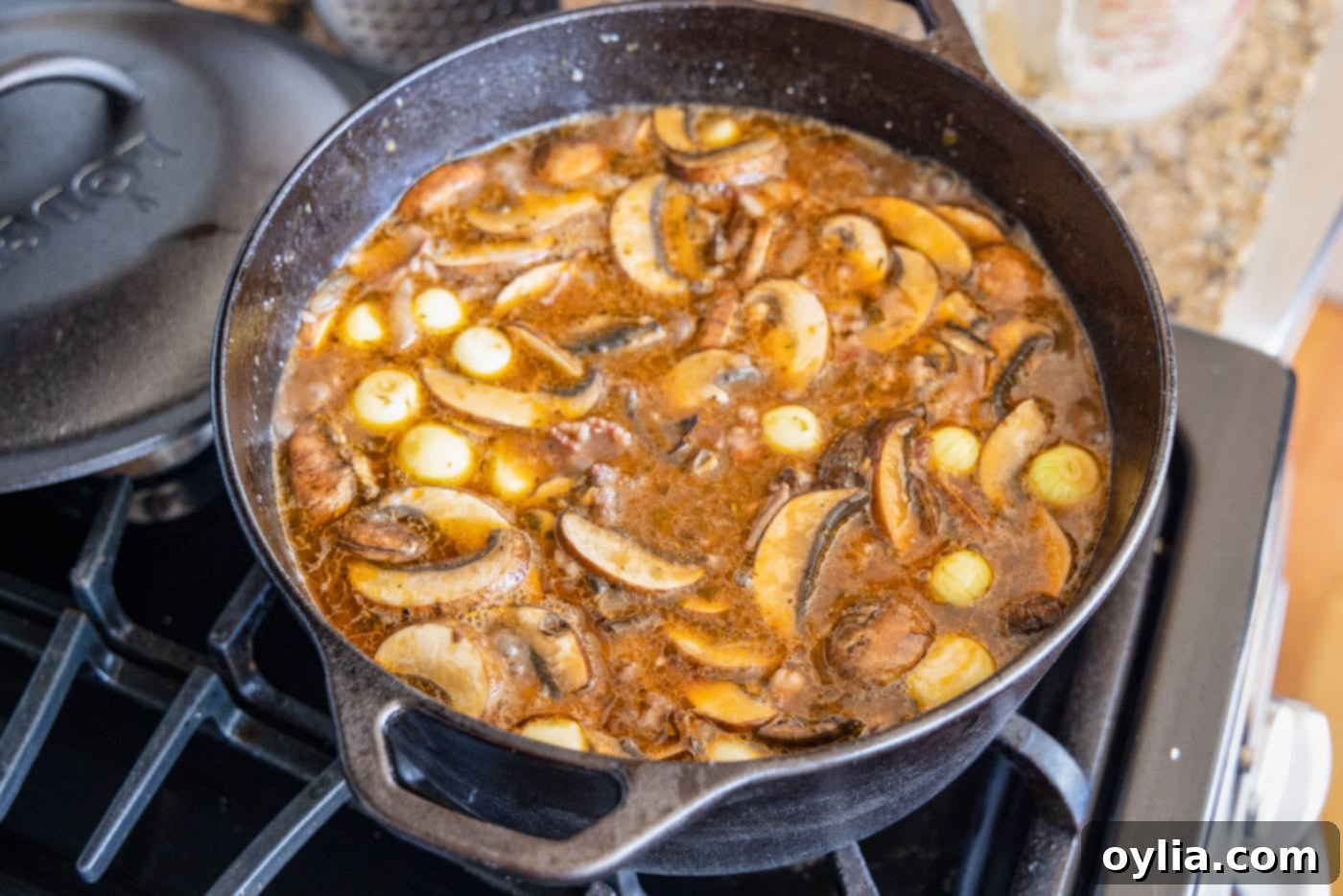 Beef Bourguignon simmering in a Dutch oven with added mushrooms and pearl onions