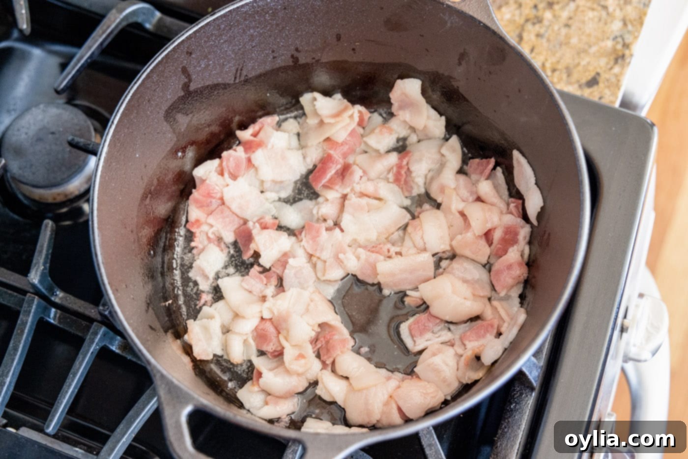 Bacon cooking in a Dutch oven with olive oil, rendering fat and becoming tender