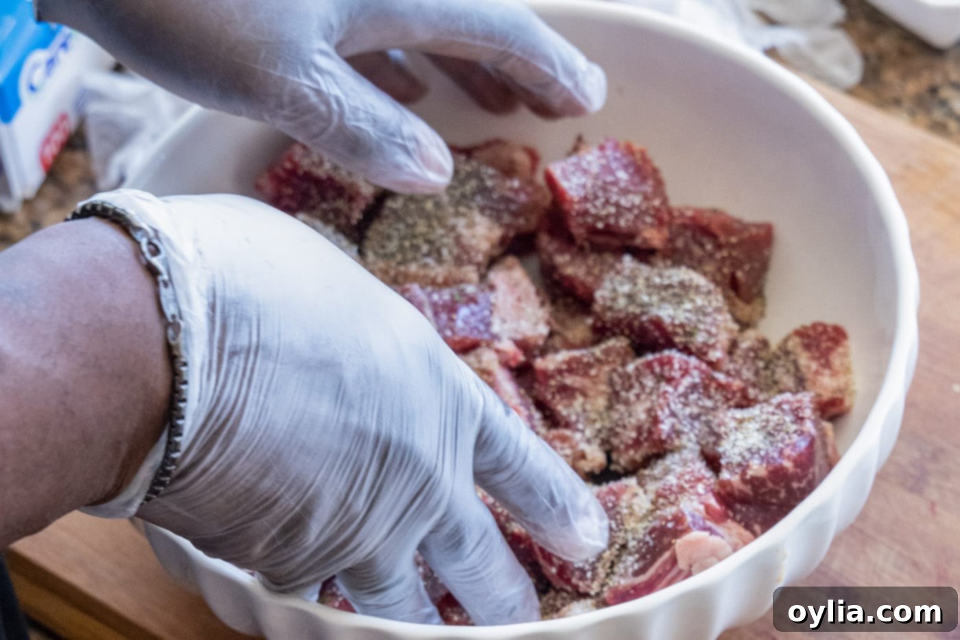 Cubed beef being seasoned with garlic salt and black pepper in a bowl