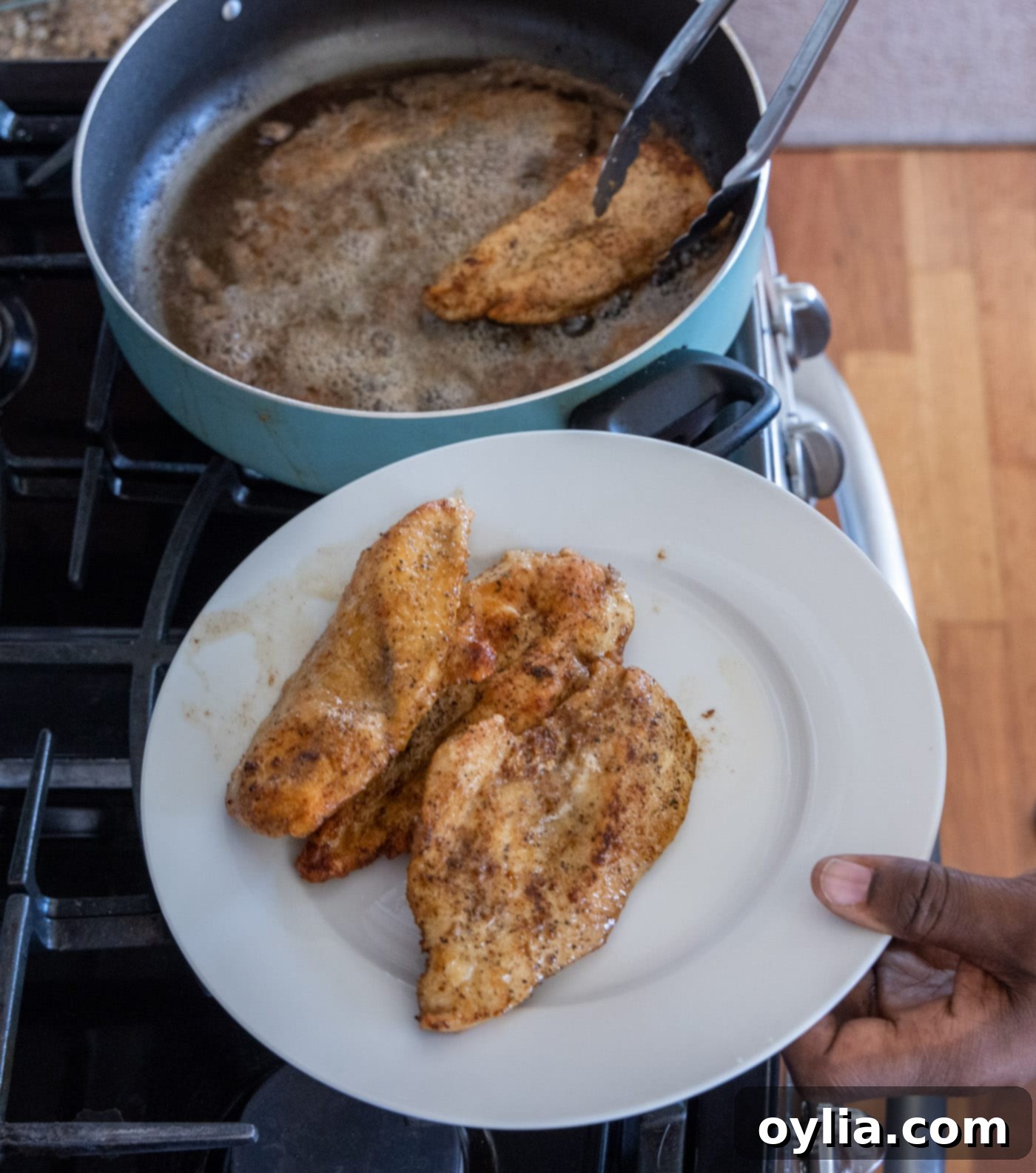 Removing golden brown chicken breasts from a skillet to a clean plate