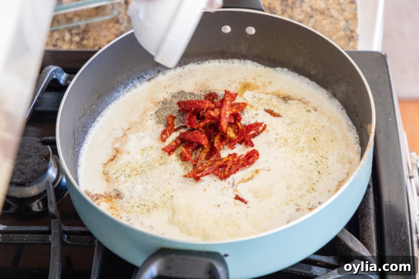 Adding sun-dried tomatoes, garlic, and seasonings to heavy cream mixture in a skillet