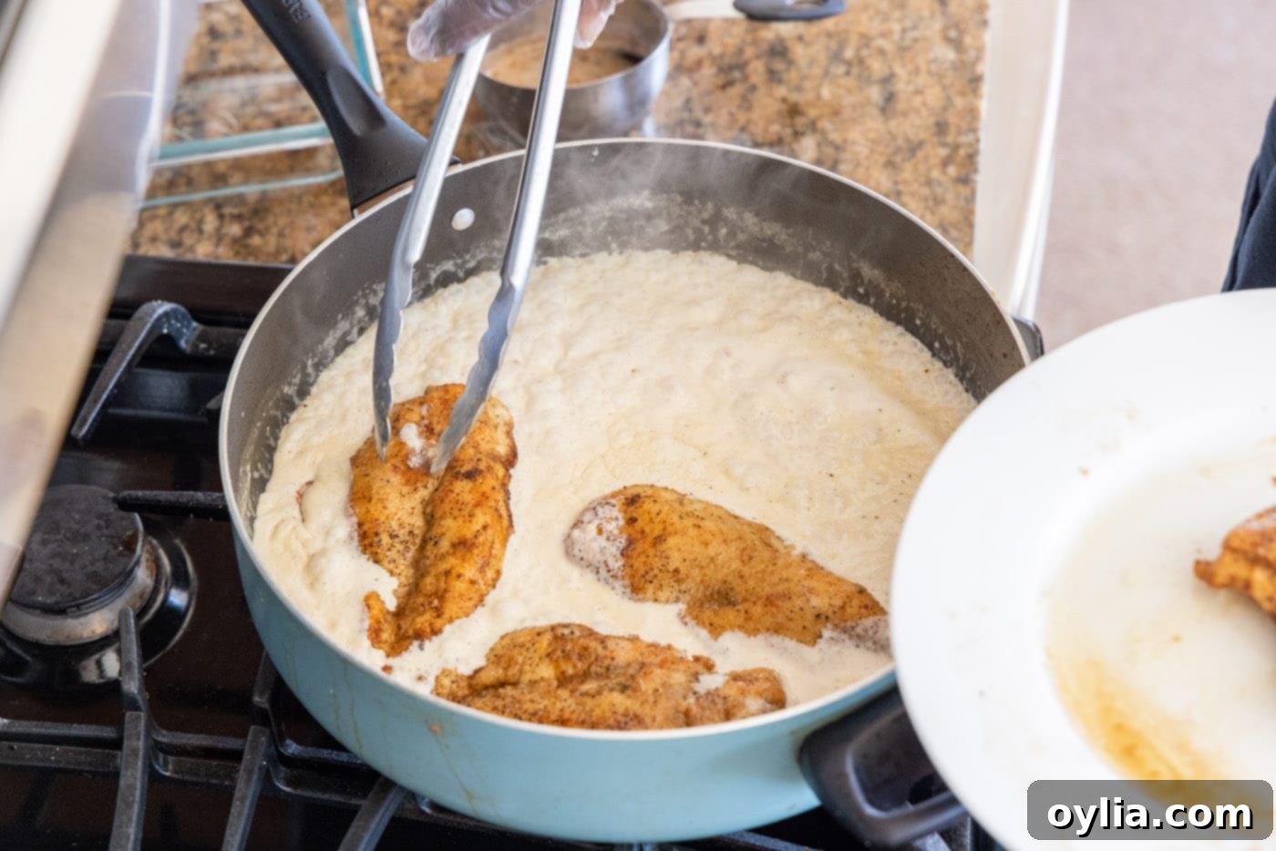 Dredging seared chicken breasts in the heavy cream sauce in a skillet, coating them evenly