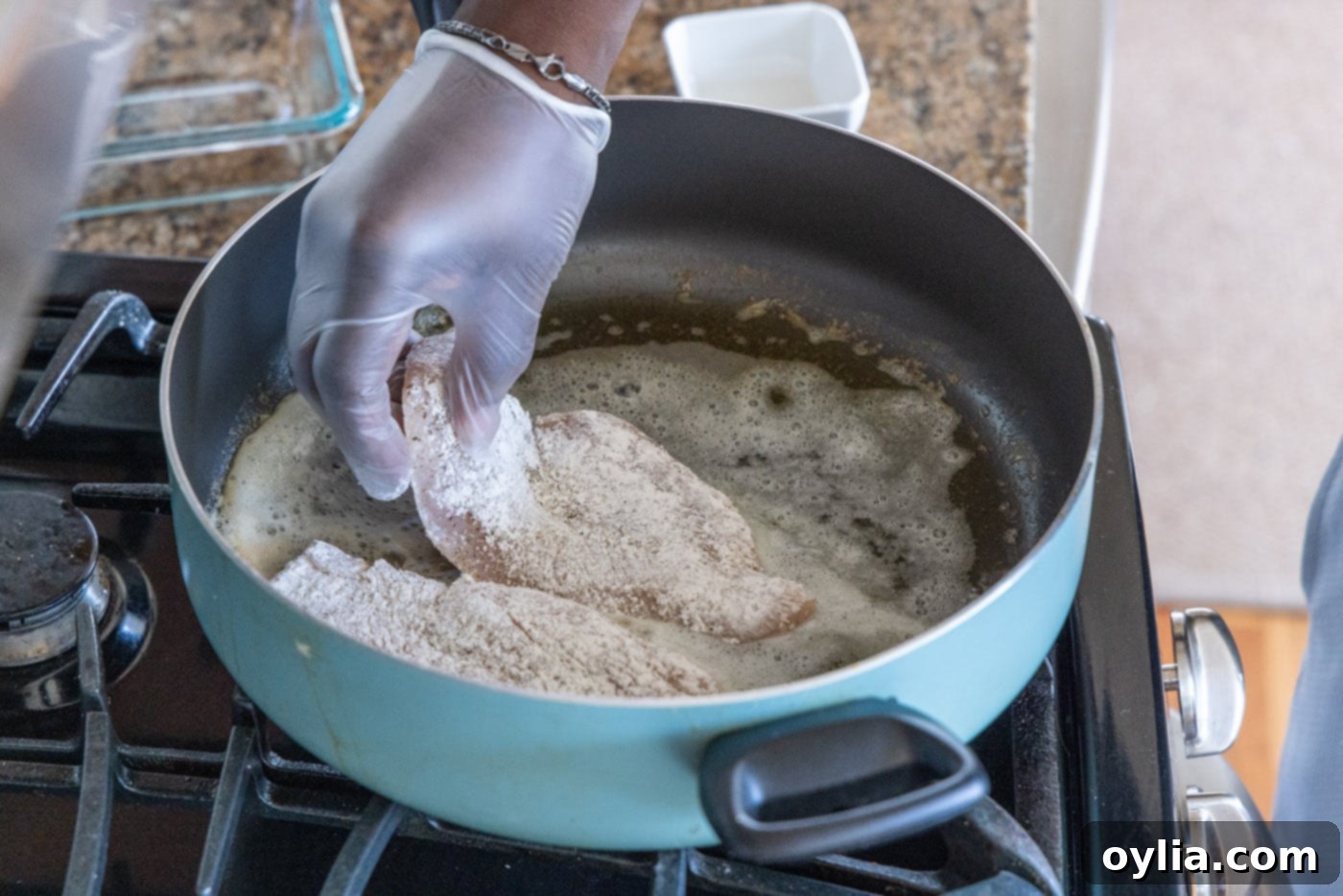 Adding flour-dredged chicken breasts to a hot skillet with melted butter and olive oil