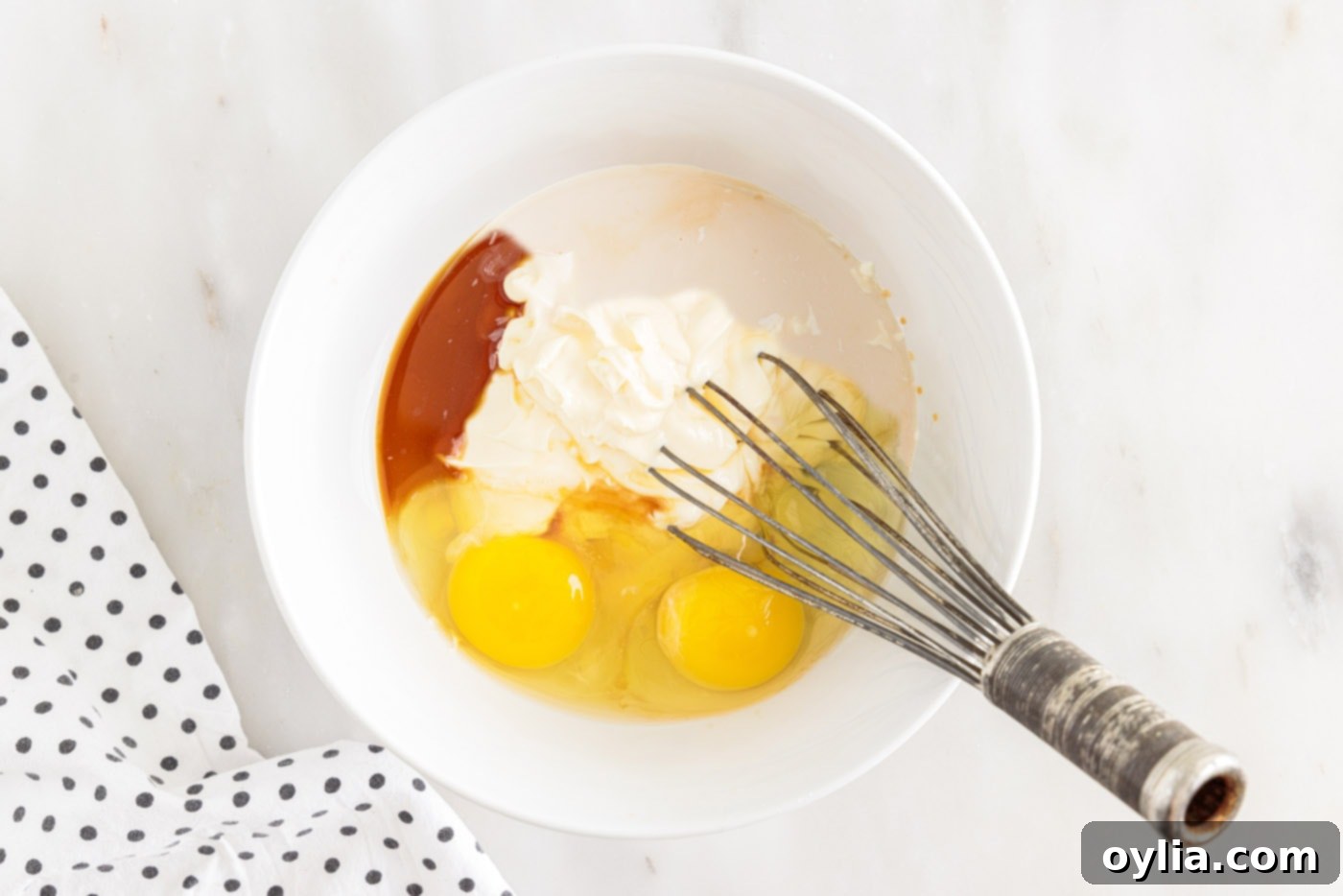whisking eggs, milk, mayonnaise, and vanilla in a bowl