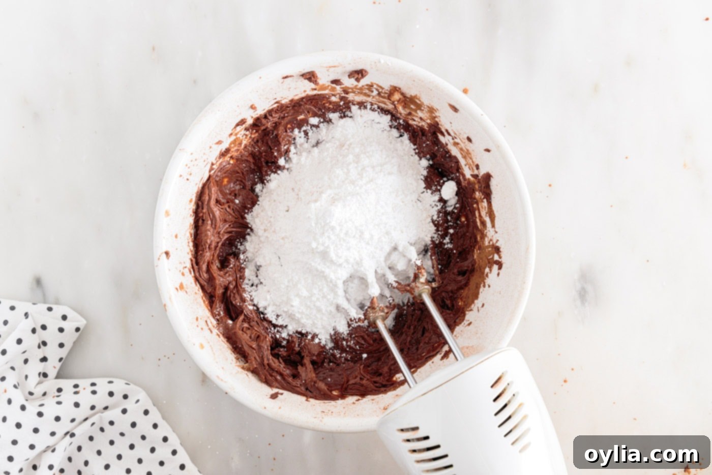 powdered sugar added to chocolate frosting ingredients in a bowl