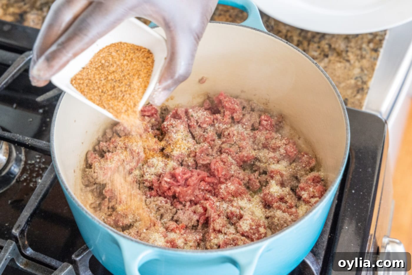 adding cajun seasoning to ground beef in a dutch oven
