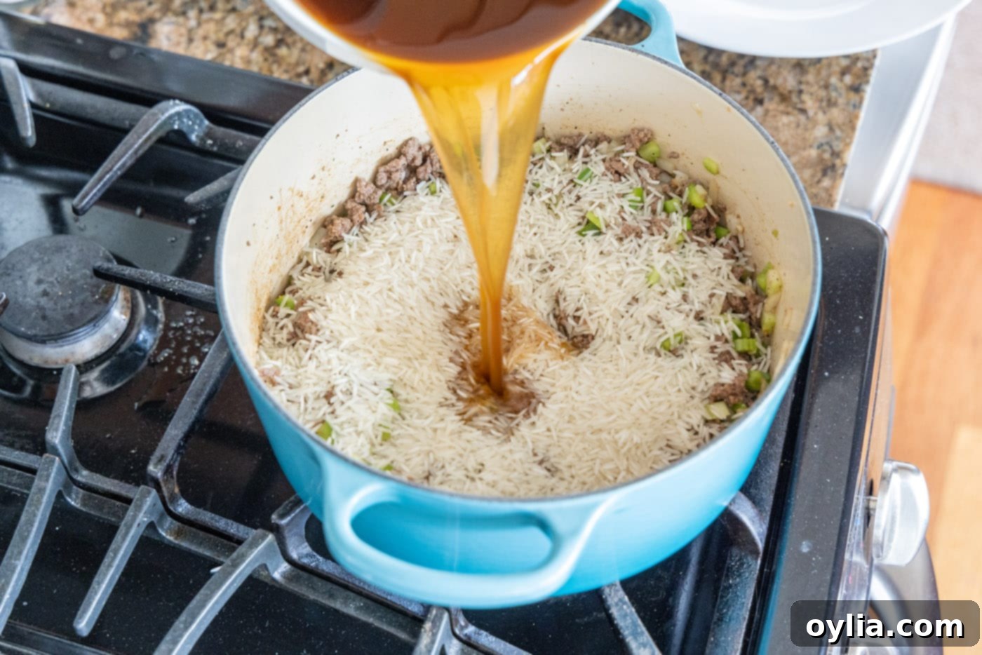 pouring beef broth over dirty rice