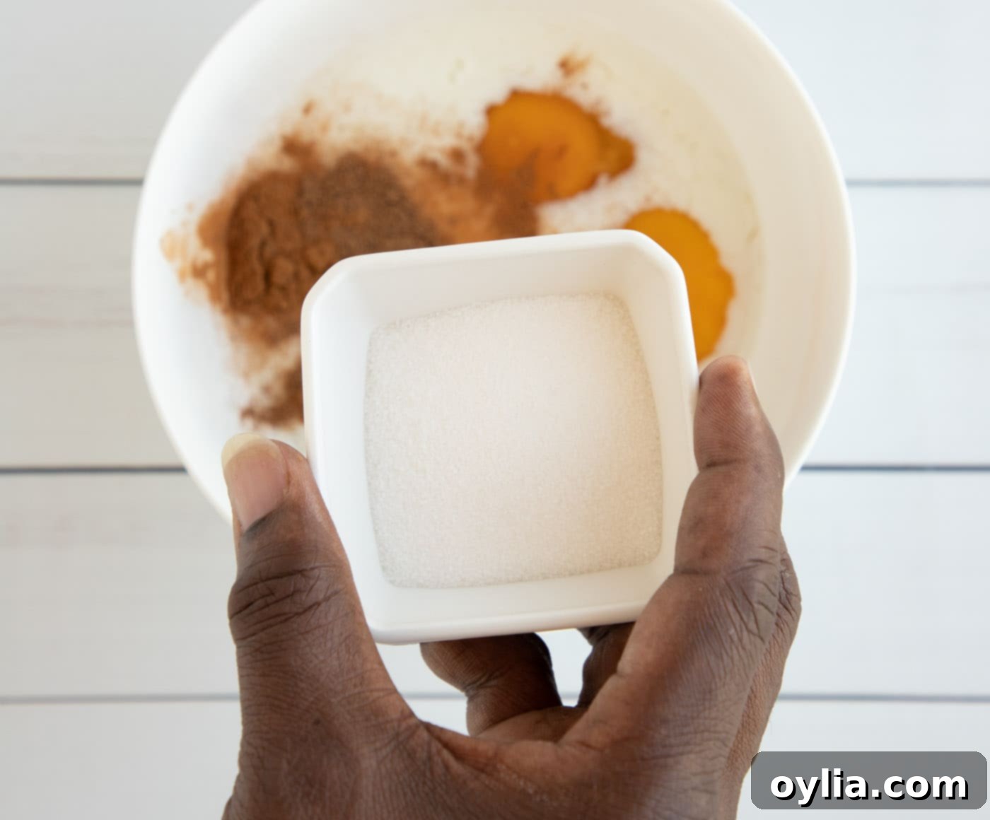 Hand holding sugar over bowl of spices and egg mixture for French toast custard
