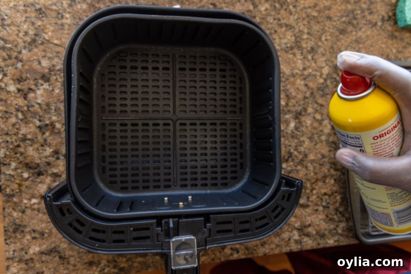 A hand spraying the inside of an air fryer basket with cooking spray, preparing it for the shrimp.