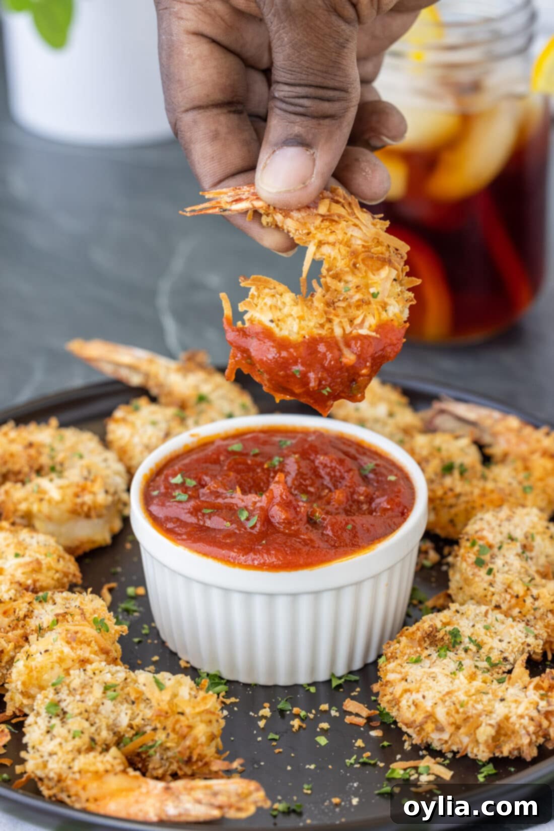 Crispy Air Fryer Coconut Shrimp being dipped into a bowl of cocktail sauce, showcasing its golden crust.