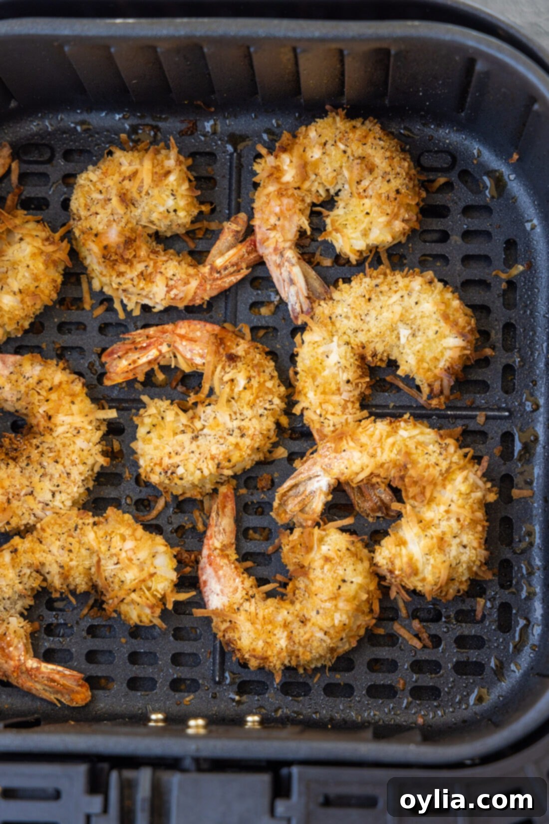 Coconut shrimp being cooked inside an air fryer basket, showing a golden crust forming.