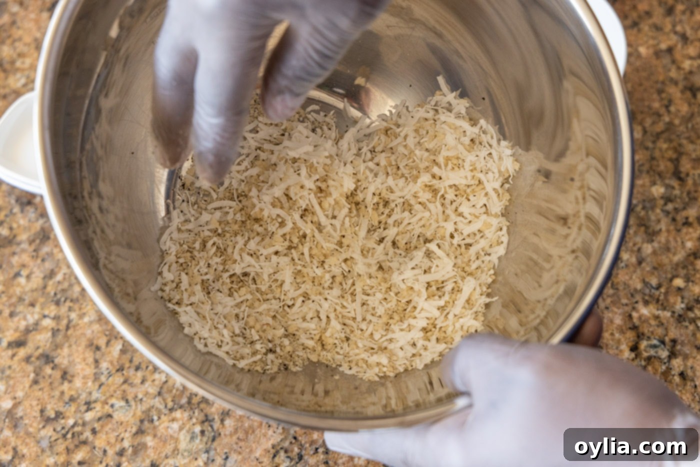 Hands gently tossing sweetened coconut flakes with panko breadcrumbs and spices in a large bowl to create the coating mixture.