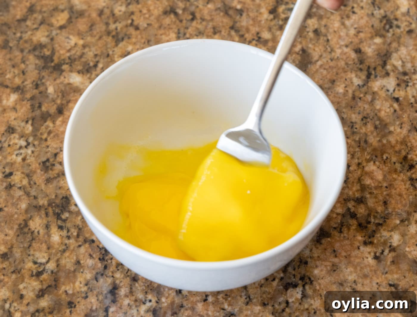 A fork whisking eggs with a small amount of water in a bowl, creating an egg wash.