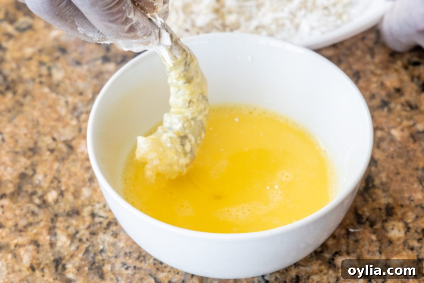 A flour-dredged shrimp being dipped into the prepared egg wash, ready for the final coating.