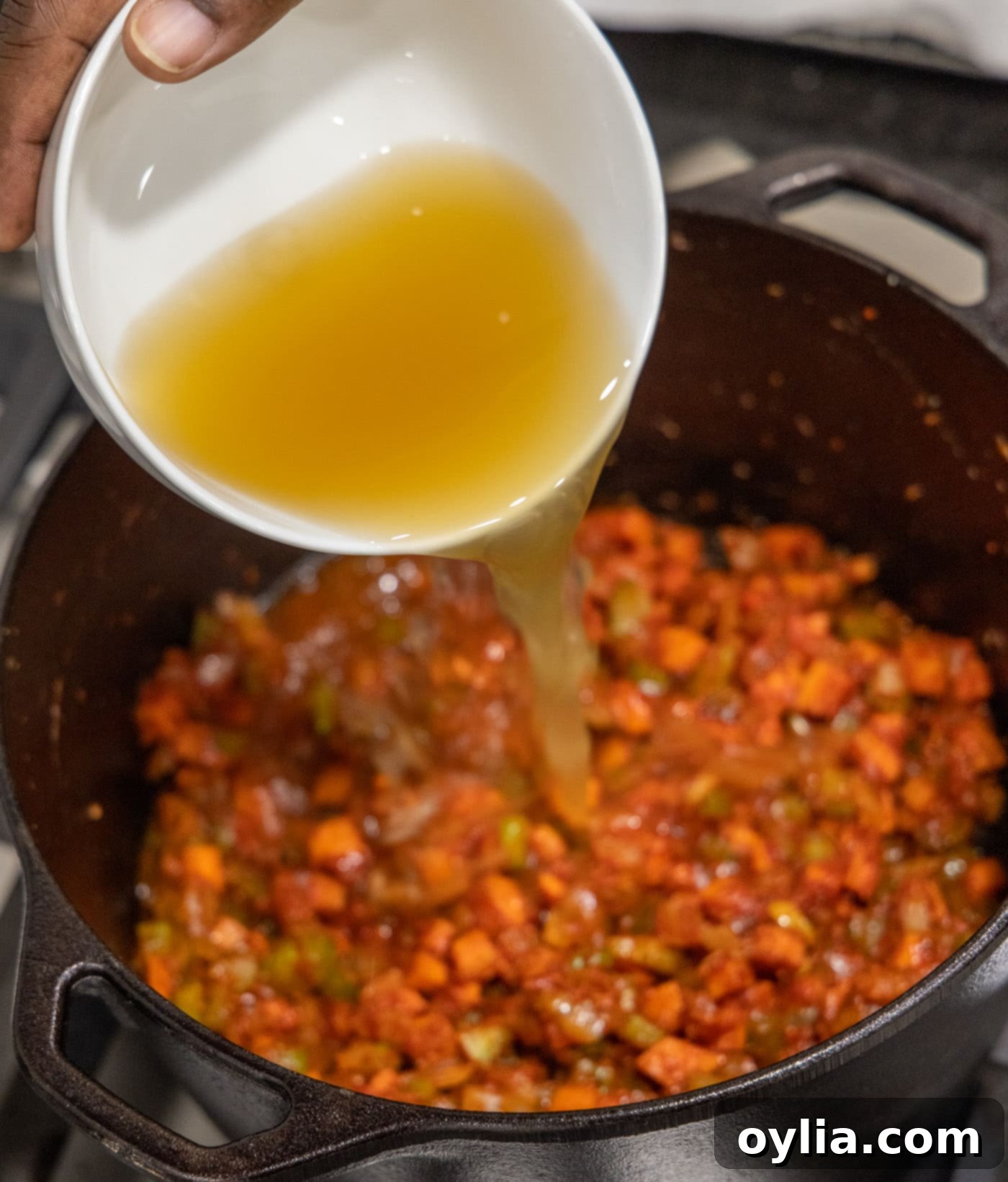 Pouring chicken broth into the simmering veal osso buco mixture