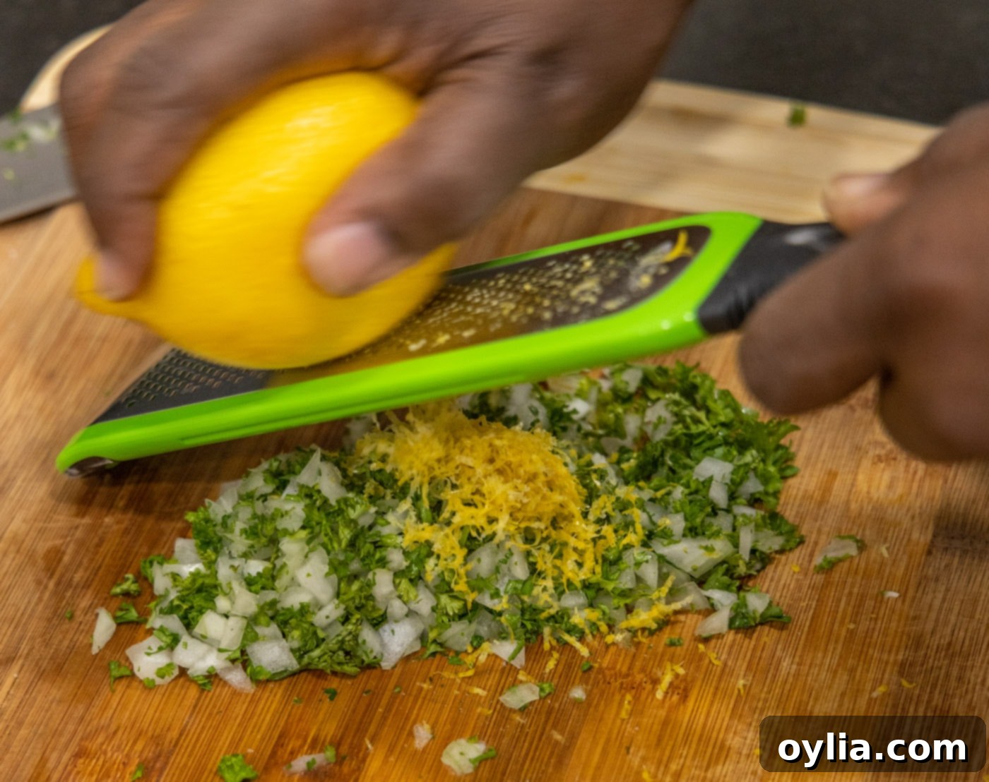 Grating fresh lemon zest over chopped onion and parsley for the gremolata