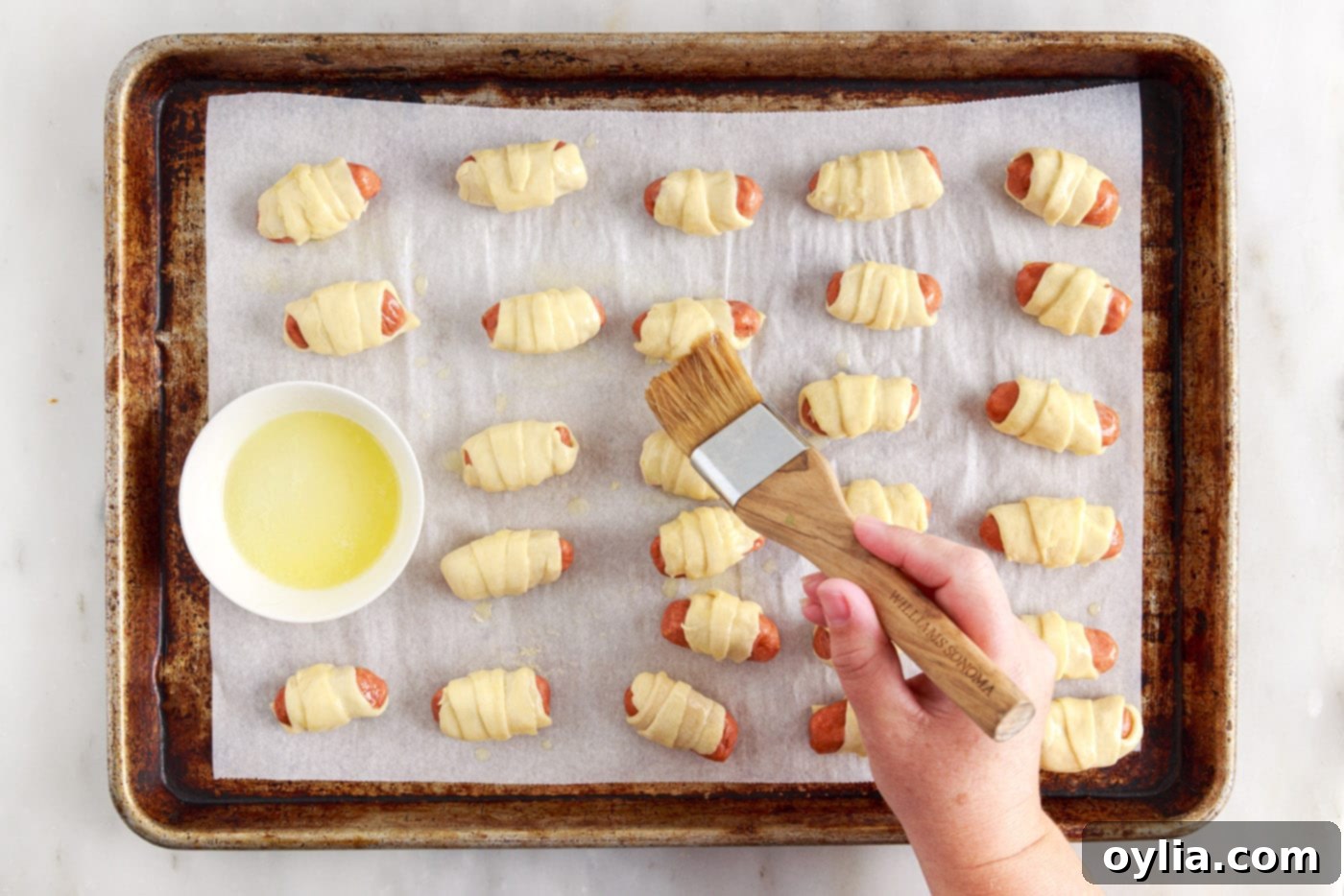 brushing pigs in a blanket with melted butter before baking