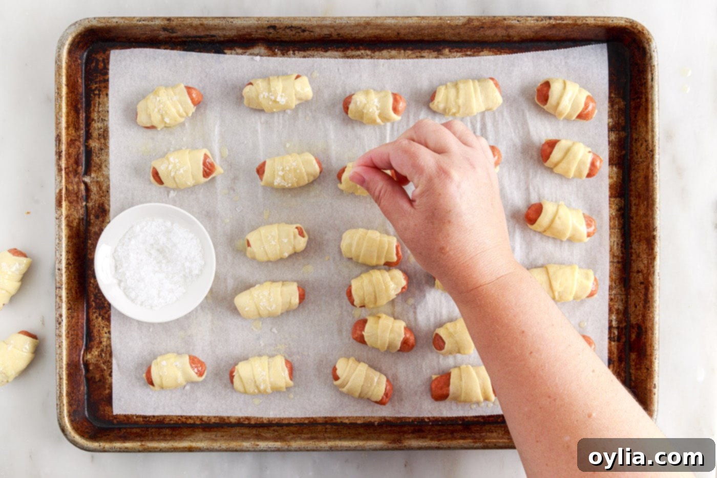 hand sprinkling flaked sea salt over buttered pigs in a blanket