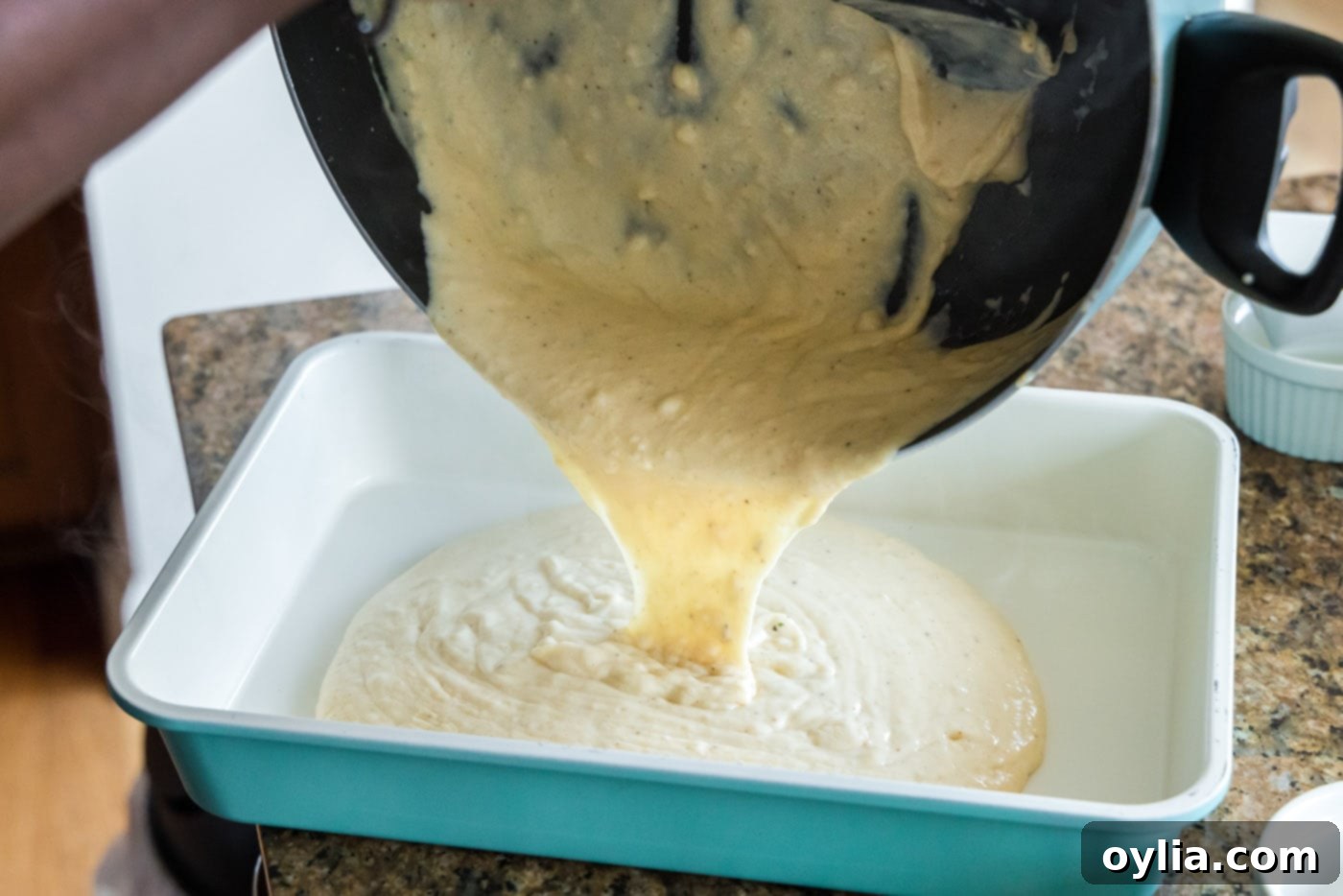 Pouring the creamy seafood sauce into the bottom of a baking dish for the first layer