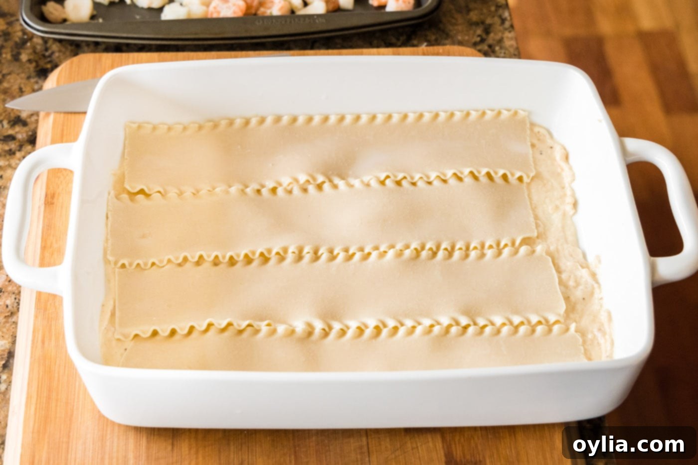 Arranging soaked lasagna noodles in a baking dish as the first pasta layer