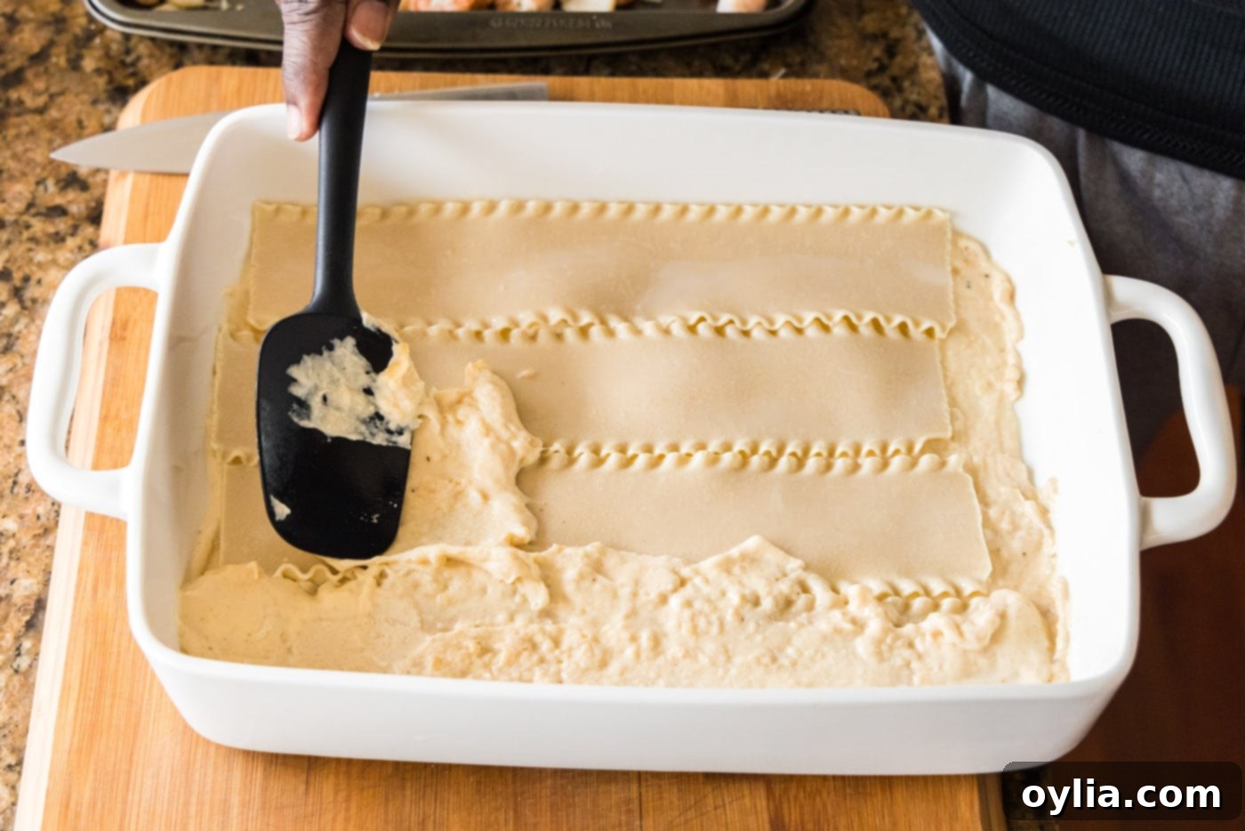 Spreading a layer of creamy sauce over the lasagna noodles