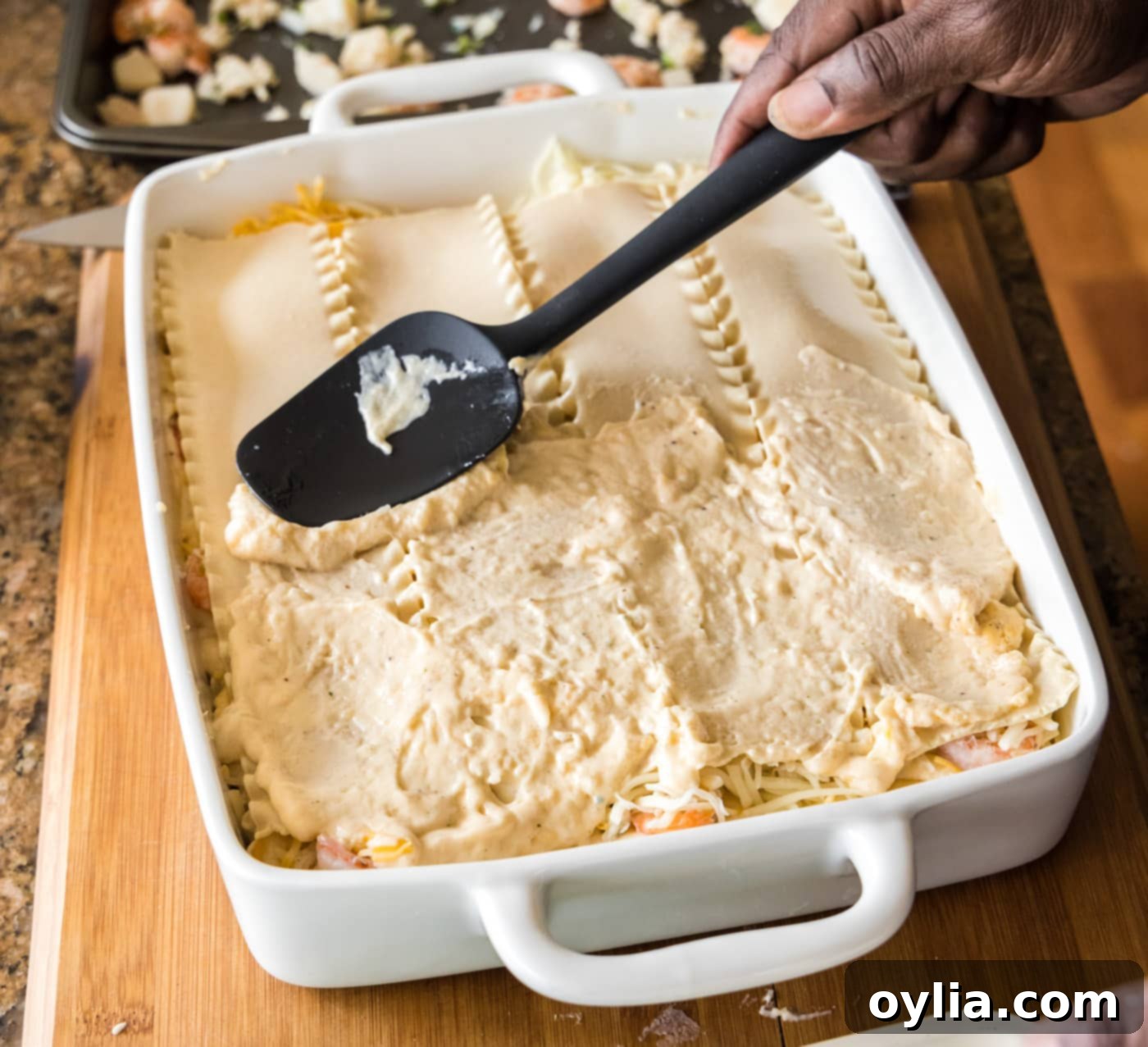 Spreading cream sauce over the second layer of lasagna noodles