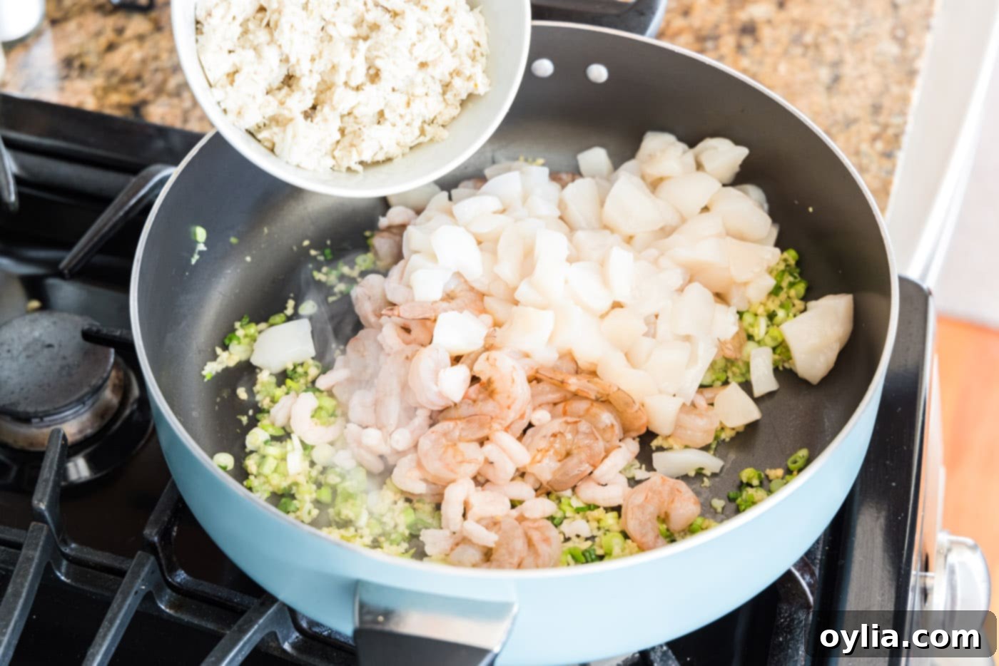 Adding green onions, garlic, and shrimp to a large skillet with various stocks for cooking