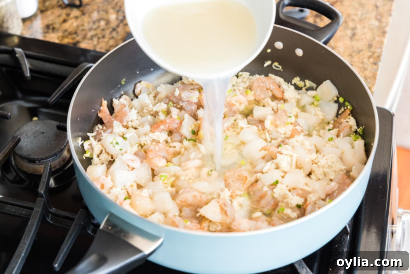 Pouring clam and seafood stock into the skillet with green onions, garlic, and shrimp
