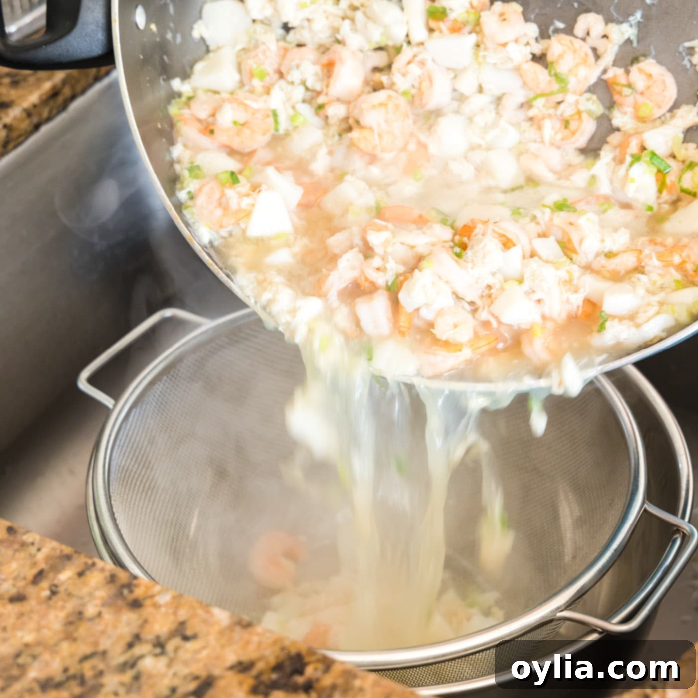 Draining cooked seafood mixture in a colander over a bowl to collect the savory stock