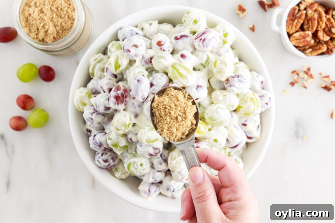 holding brown sugar over bowl of grape salad