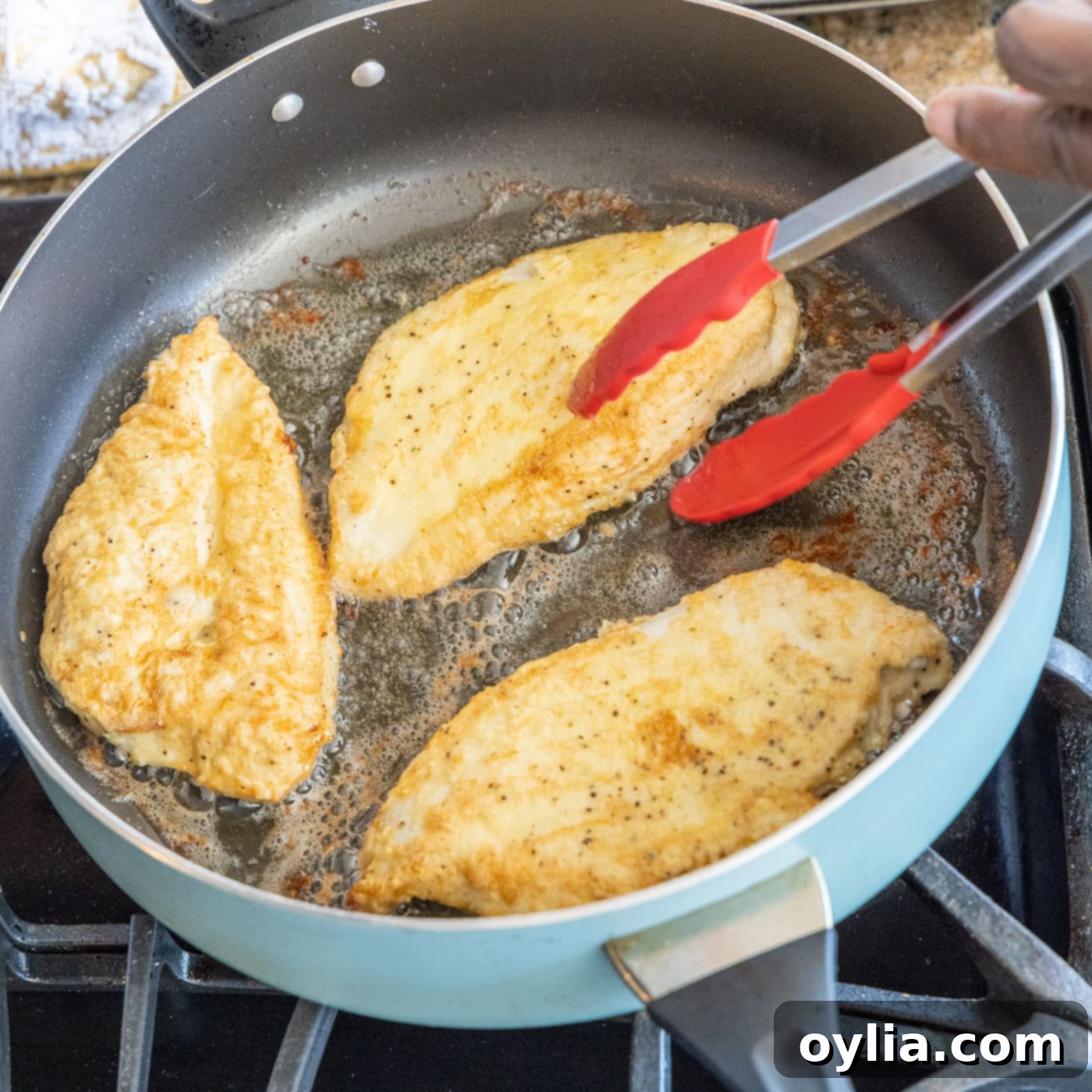 chicken breasts in a skillet with tongs